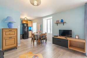 A modern living room with a dining area, a kitchen in the background, and a TV on a wooden stand. - Furnished Apartment in Townhouse, City Center Location (Jonzac)
