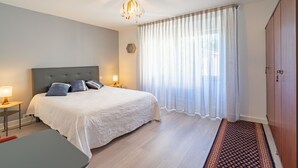 A bedroom with a bed, bedside lamps, a rug, a wardrobe, and a window with curtains. - Furnished Apartment in Townhouse, City Center Location (Jonzac)
