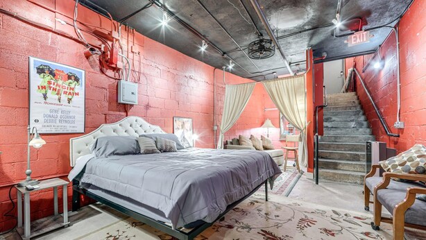 A bedroom with a bed, a nightstand, a chair, a staircase, and a poster on the wall. - Cozy Single at The Strand (Waynesville)