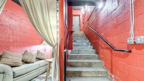 A staircase with a red wall, a beige curtain, and a sofa with pillows. - Cozy Single at The Strand (Waynesville)