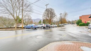 A street view with cars parked on the side, a stop sign, and a building in the background. - Cozy Single at The Strand (Waynesville)