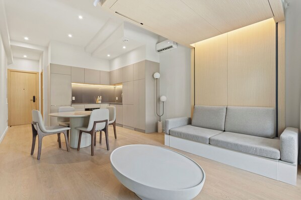 Ein modernes Wohnzimmer mit einer Couch, einem Esstisch mit Stühlen und einer Küchenzeile im Hintergrund.