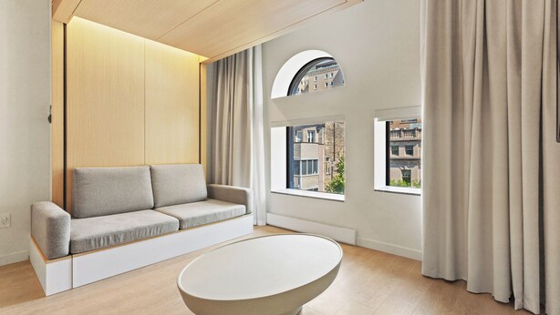 Una sala de estar moderna con sofá, mesa de centro y ventanas amplias con vistas a edificios.