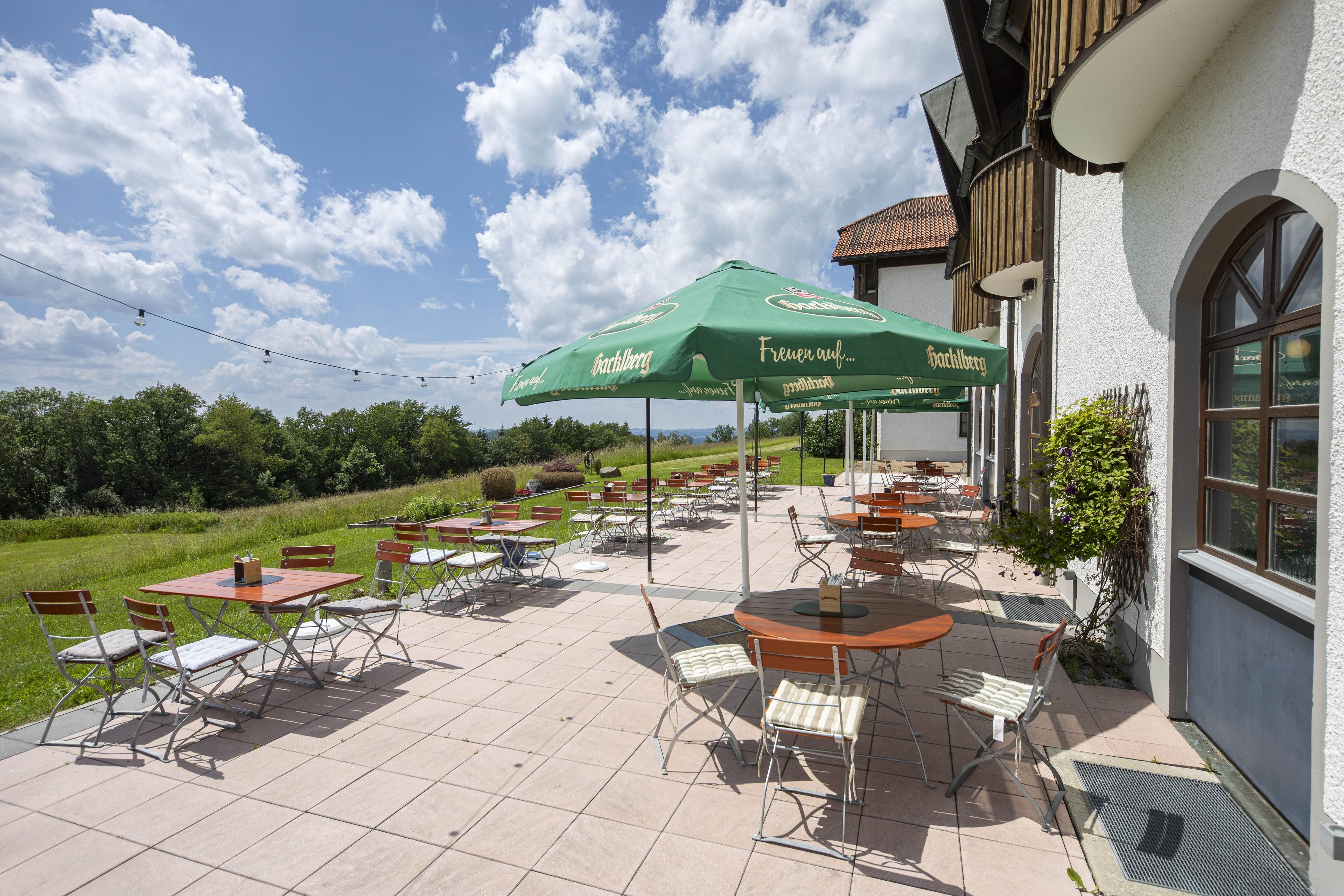 An outdoor patio with tables and chairs, green umbrellas, and a view of the countryside.