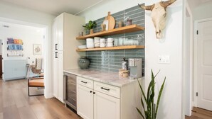 Une cuisine moderne avec des meubles blancs, un plan de travail en marbre et une étagère murale originale où sont rangés les ustensiles de cuisine.