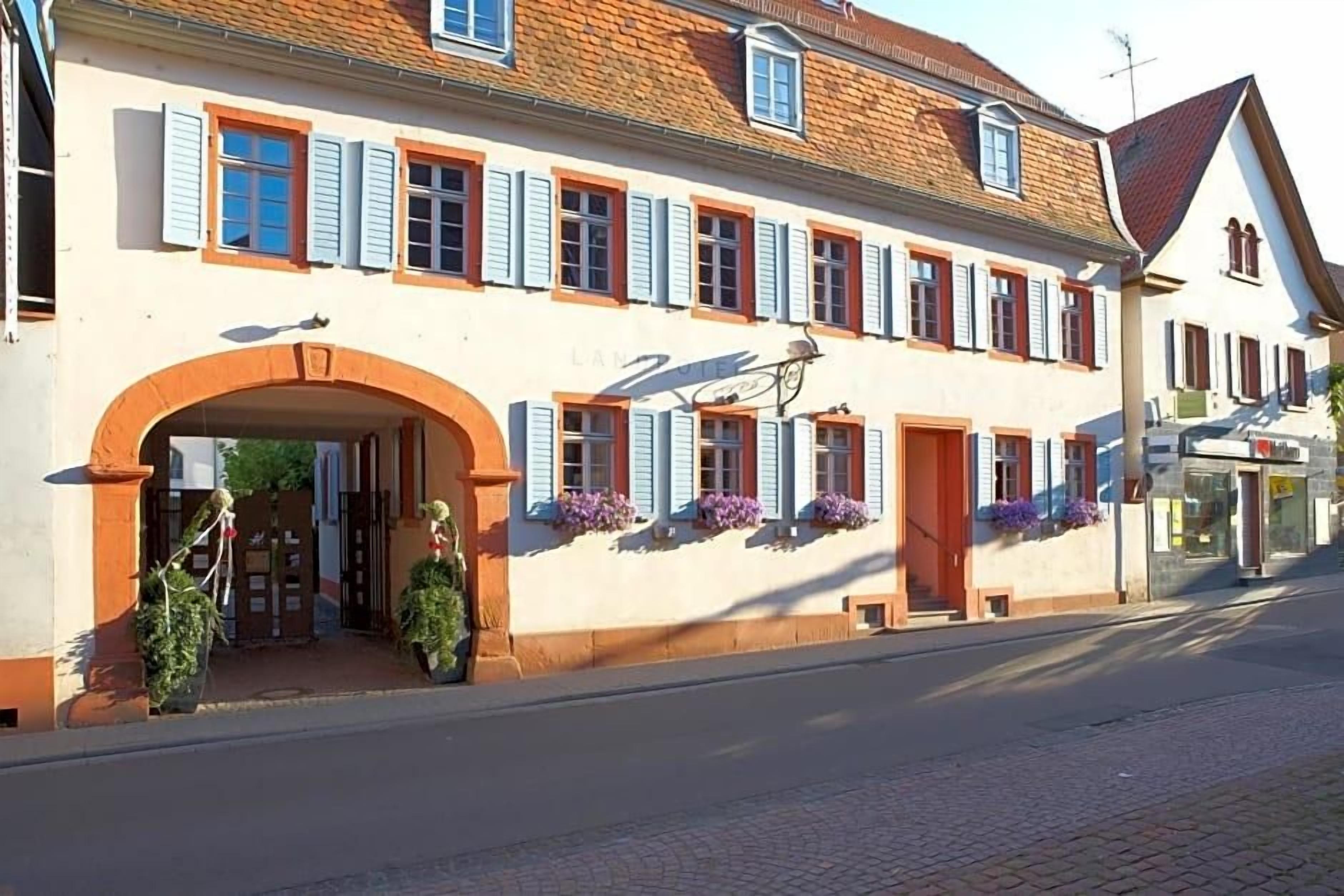A traditional European building with a central archway, multiple windows with shutters, and flower boxes on the facade.