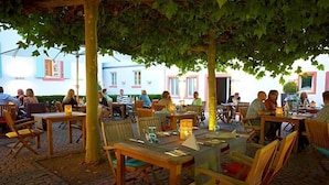 Un café al aire libre con mesas y sillas de madera, rodeado de árboles.