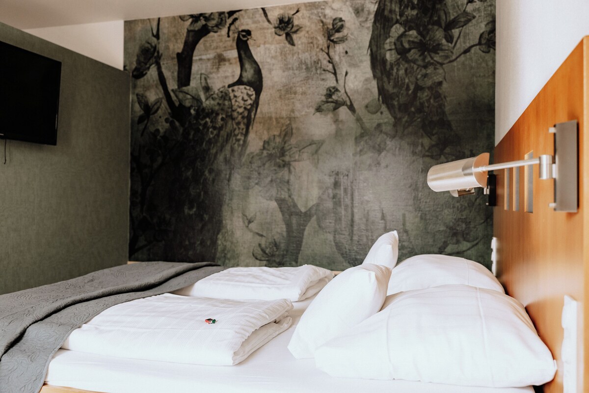 A neatly made bed with white linens and pillows, a gray blanket, and a wall-mounted lamp.