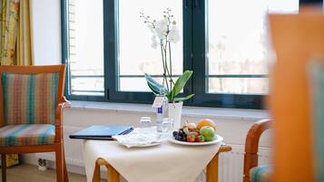 A dining table with a laptop, a plate of fruit, a vase with flowers, and a window with curtains.