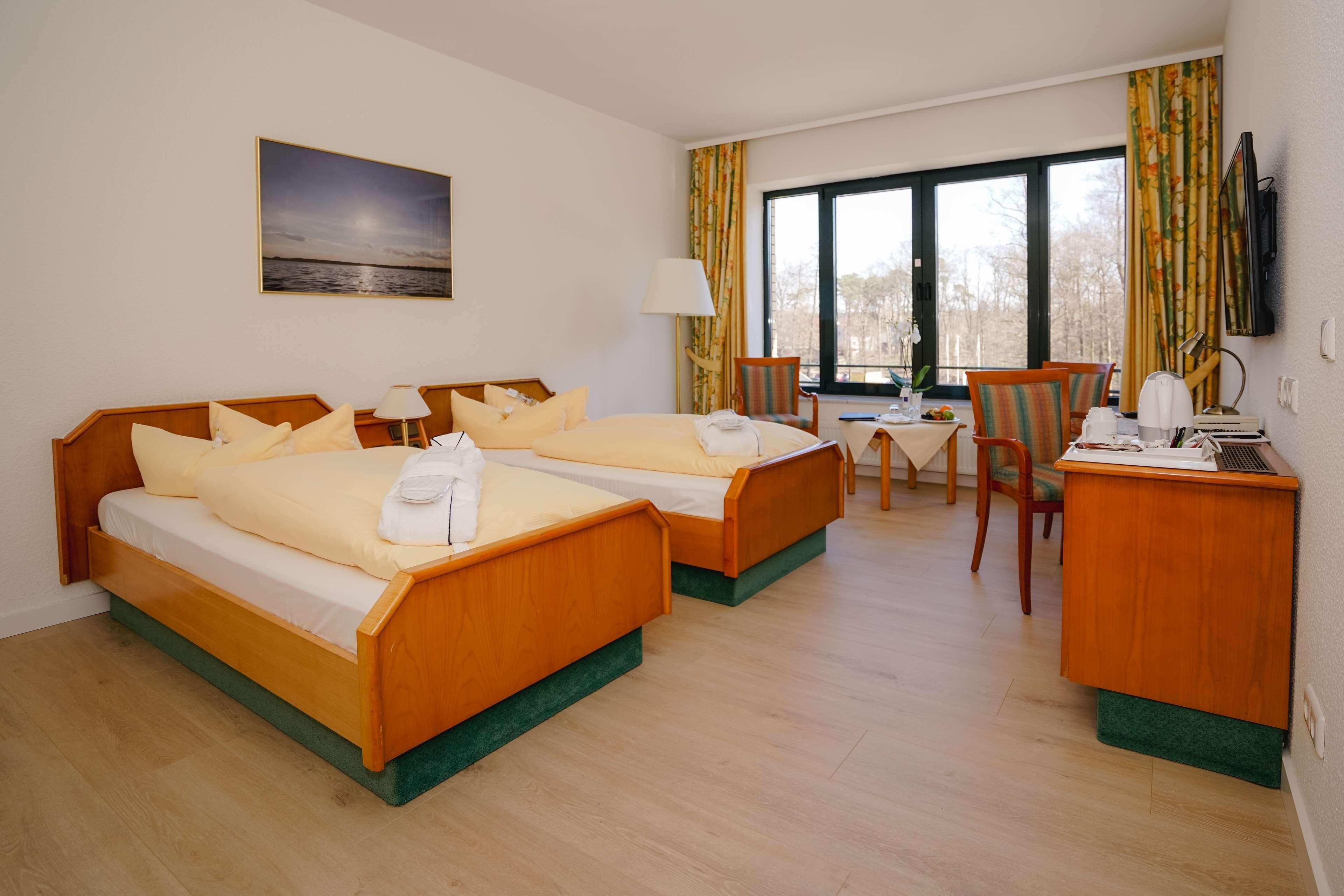 A hotel room with two beds, a desk, a chair, a TV, and a window with curtains.