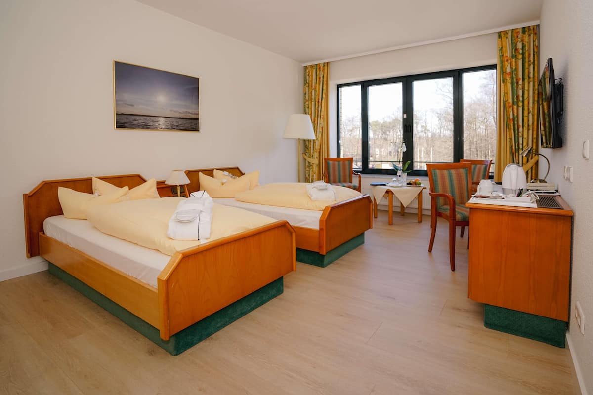 Une chambre d’hôtel avec deux lits, un bureau, une chaise, une télévision et une fenêtre avec des rideaux.