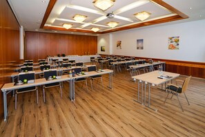 Ein Konferenzraum mit mehreren Tischen und Stühlen, Holzböden und Deckenleuchten.