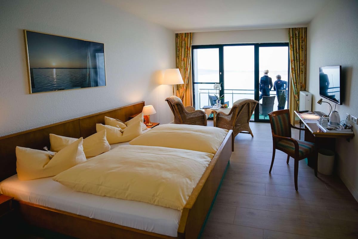 Une chambre d’hôtel avec un grand lit, un bureau, une chaise, une télévision et une vue sur la mer par la fenêtre.