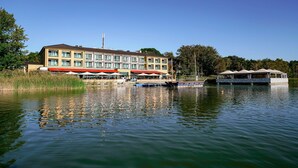 A hotel with a large building, outdoor seating, and boats on the water. - TOP Countryline Seebad Casino (Rangsdorf)