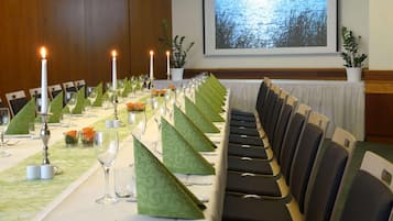 A long dining table set with candles, green napkins, and wine glasses, with chairs aligned along one side.