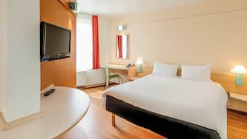 Ein Hotelzimmer mit Bett, Schreibtisch, Stuhl und Fernseher.