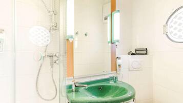 A bathroom with a glass-enclosed shower, a green sink, a white toilet, and a mirror with a wooden frame.
