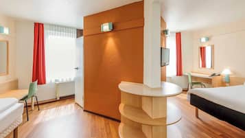 A hotel room with a bed, a desk, a chair, a round wooden table, and a TV mounted on the wall.