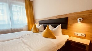Una habitación de hotel con una cama, dos almohadas, una mesita de noche y una lámpara de pared.