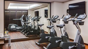 A gym with multiple stationary bikes, a treadmill, and a mirror reflecting the room. - Dorint Parkhotel Meissen (Nossen)