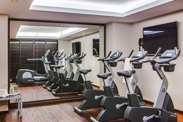 Un gimnasio con varias bicicletas estáticas, una cinta de correr y un espejo que refleja el espacio.
