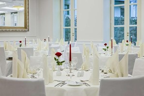 Un salón de banquetes con mesas redondas dispuestas para un evento formal, con manteles y servilletas blancos y velas rojas.