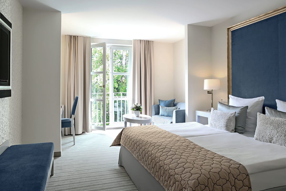 A hotel room with a large bed, a seating area with a table and chairs, and a view through a glass door.