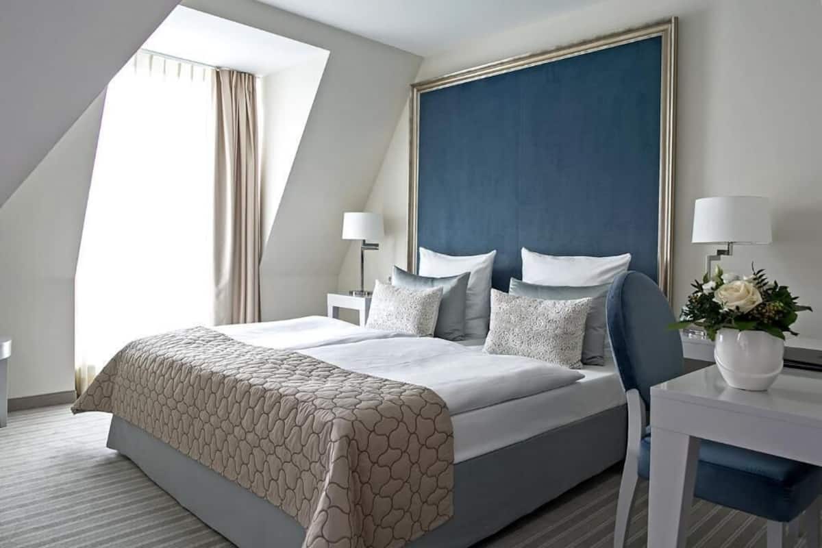 A modern hotel room with a large bed, a desk, and a window with curtains.