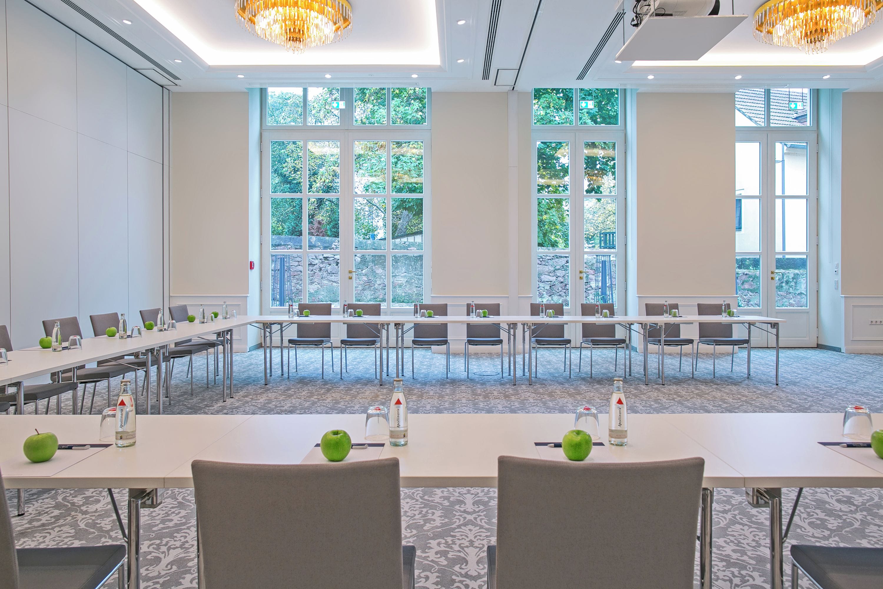 Un salón de conferencias con largas mesas, sillas y manzanas verdes en cada una.
