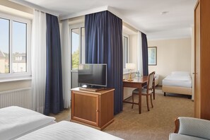 Ein Hotelzimmer mit Bett, Schreibtisch mit Stuhl, Fernseher und einem Vorhangfenster.