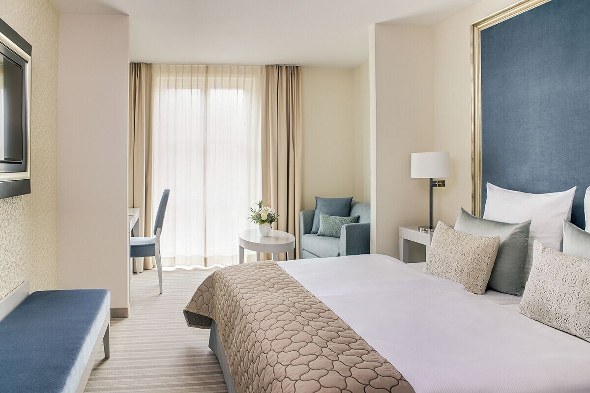 A hotel room with a large bed, a desk, a chair, and a television.
