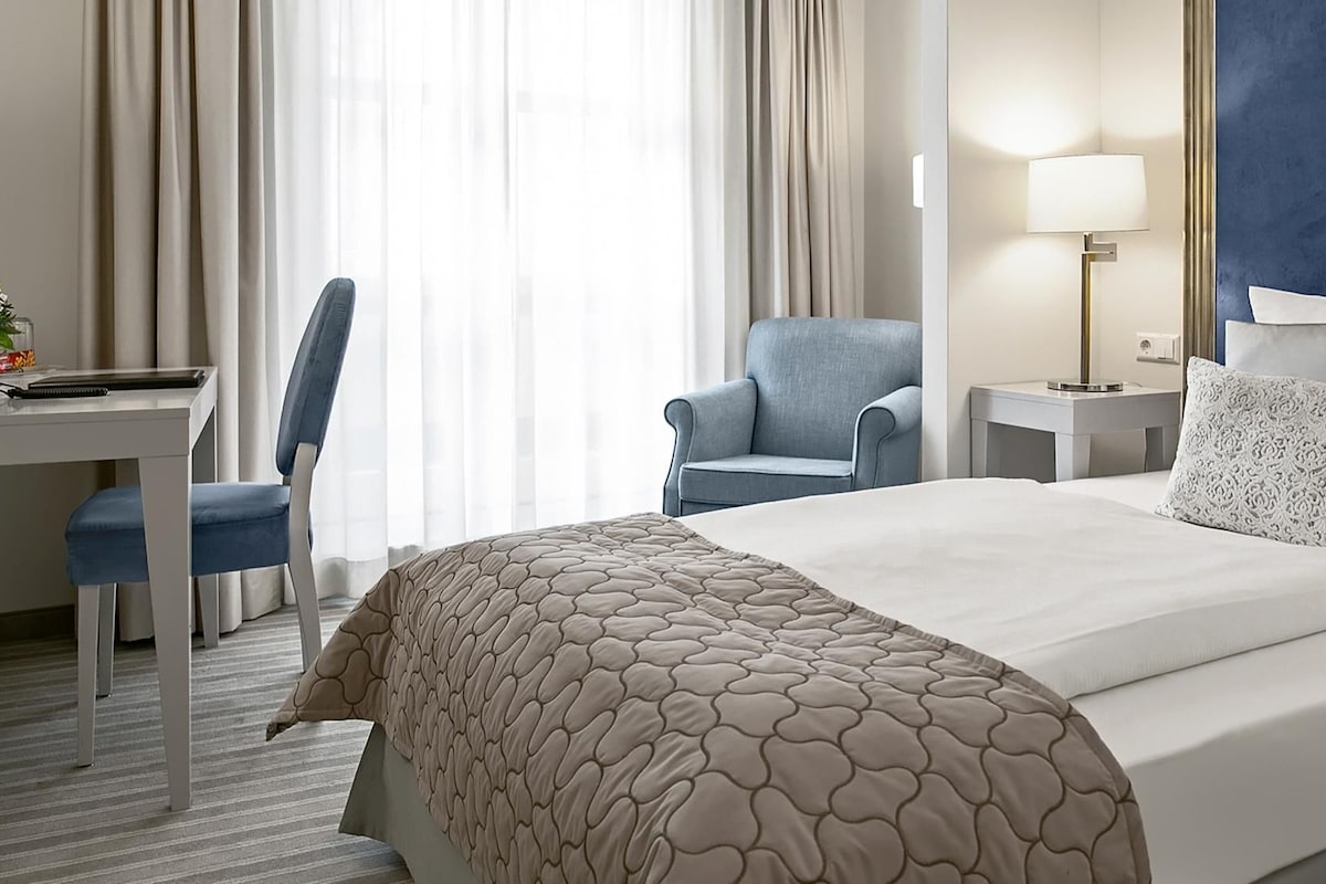 Une chambre d’hôtel comprenant un lit, un bureau, une chaise, une lampe et une table de chevet.