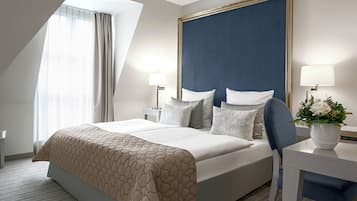 A hotel room with a large bed, two bedside tables, a desk, a chair, a window with curtains, and a wall-mounted lamp.