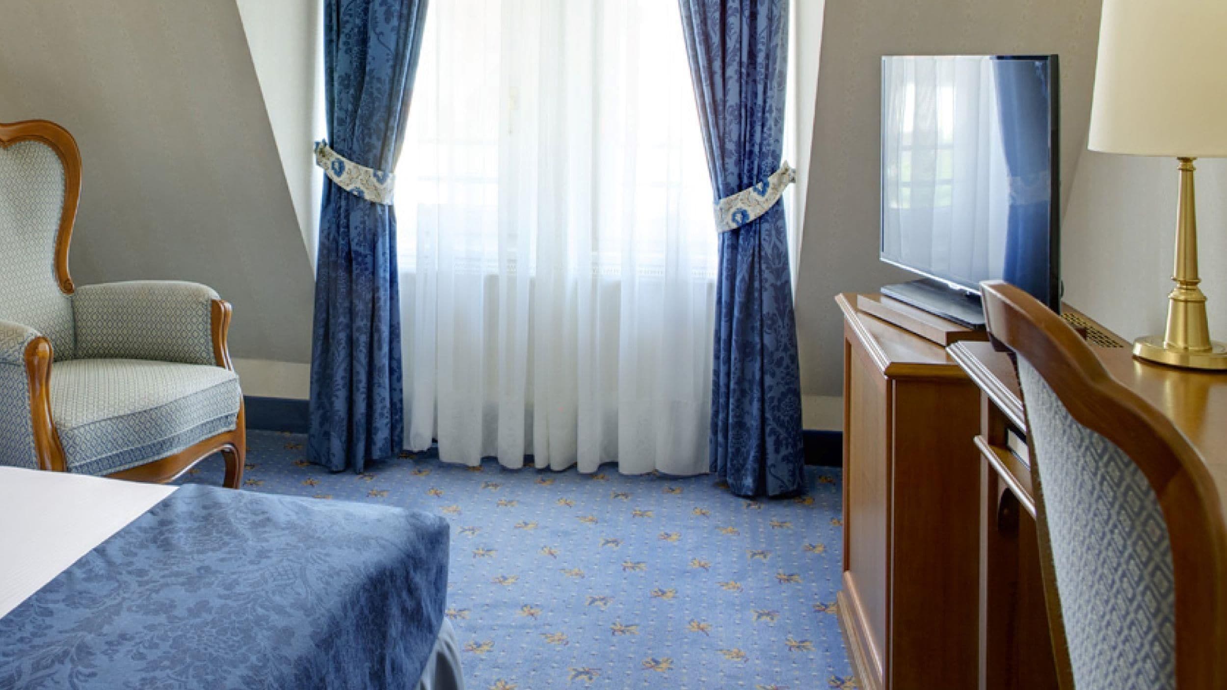 Une chambre d’hôtel avec un lit, une chaise, un bureau avec une lampe et un téléviseur.