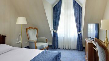Une chambre d’hôtel avec un lit, une chaise, un bureau avec une télévision et une fenêtre avec des rideaux.