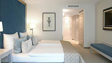 A hotel room with a bed, bedside tables, a lamp, a framed picture, a bench, and a door leading to a bathroom.