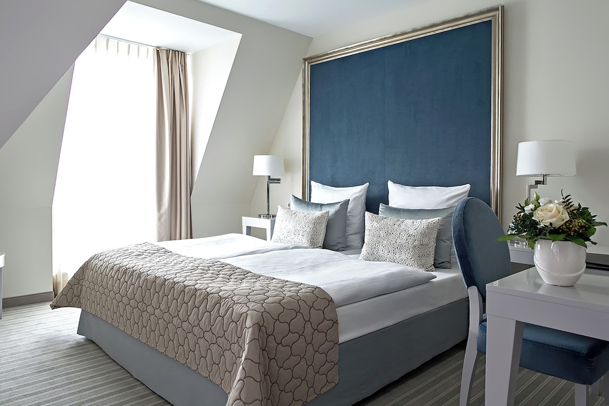Une chambre d’hôtel moderne avec un grand lit, une table de chevet, un bureau et une fenêtre avec des rideaux.