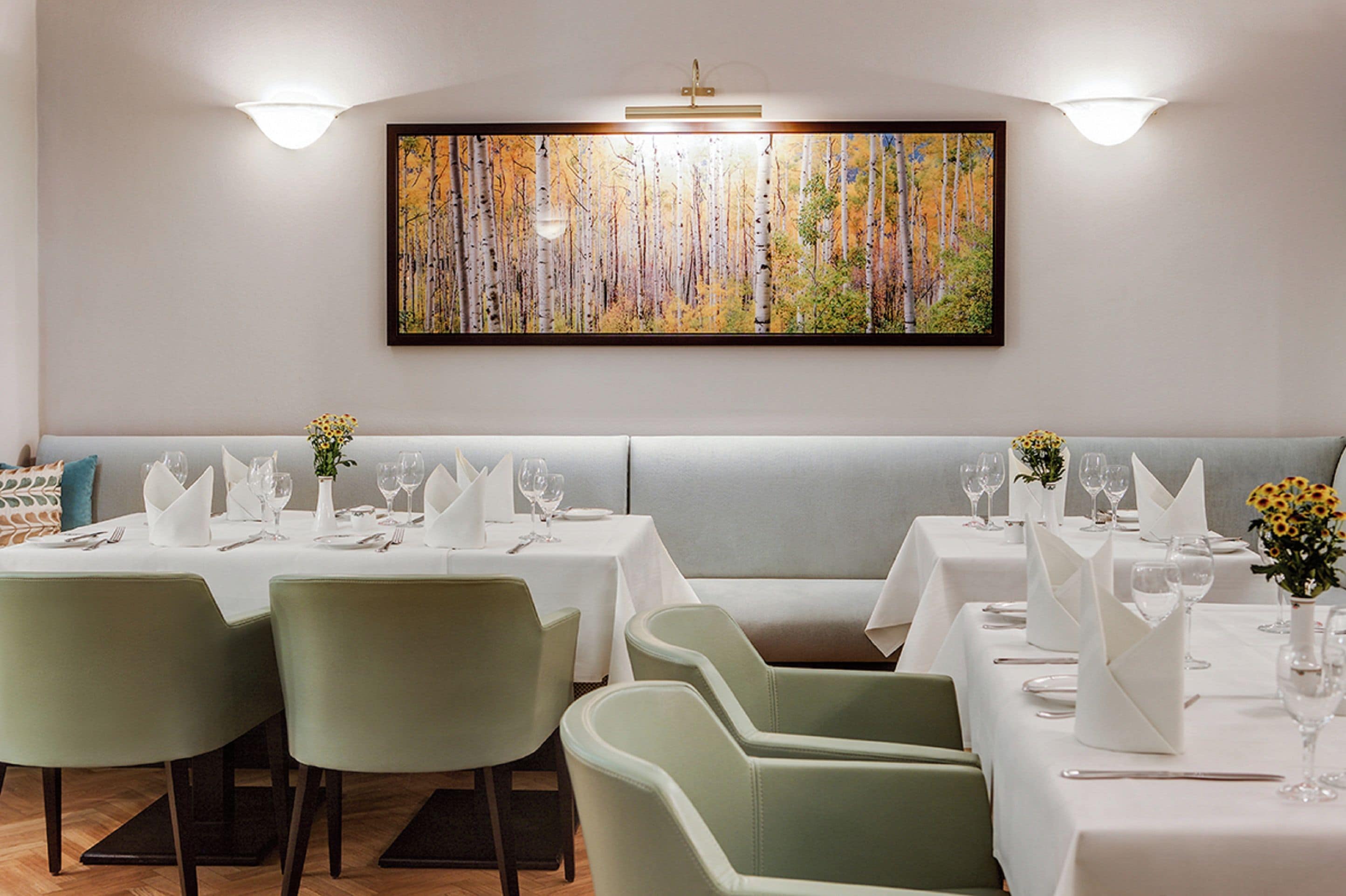 Un restaurant au décor moderne, avec une longue table à manger entourée de chaises, un espace salon avec des banquettes et un grand tableau accroché au mur.