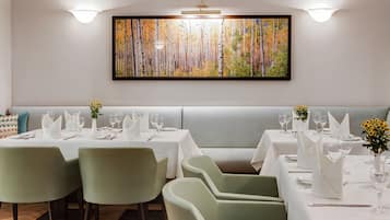 Un restaurant au décor moderne, avec une longue table à manger entourée de chaises, un espace salon avec des banquettes et un grand tableau accroché au mur.