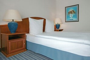 A hotel room with a bed, two bedside tables with lamps, a wooden nightstand, a framed picture on the wall, and a striped carpet. - Dorint Parkhotel Meissen (Nossen)