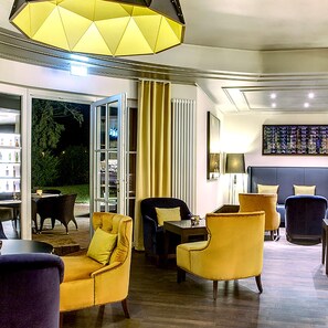 Un hall d’hôtel moderne avec un espace salon comprenant des fauteuils jaunes et un canapé foncé. Une grande fenêtre offre une vue sur la verdure environnante.