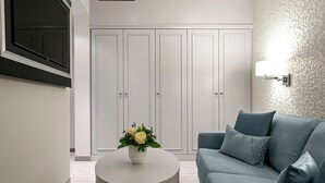 Un salon moderne avec un canapé gris, une table basse ronde blanche agrémentée d’un arrangement floral, et une armoire blanche à deux portes.
