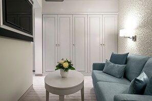 A modern living room with a grey sofa, a round white coffee table with a floral centerpiece, and a white wardrobe with two doors. - Dorint Parkhotel Meissen (Nossen)