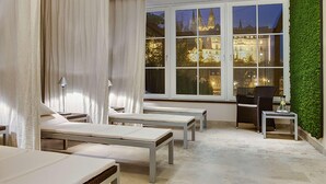 Une salle de spa équipée de fauteuils inclinables, d’une petite table et offrant une vue sur un château à travers de grandes fenêtres.