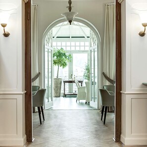 Un couloir doté d’un sol blanc, d’une grande porte en arc de cercle et donnant sur un espace extérieur aménagé avec une table et des chaises.