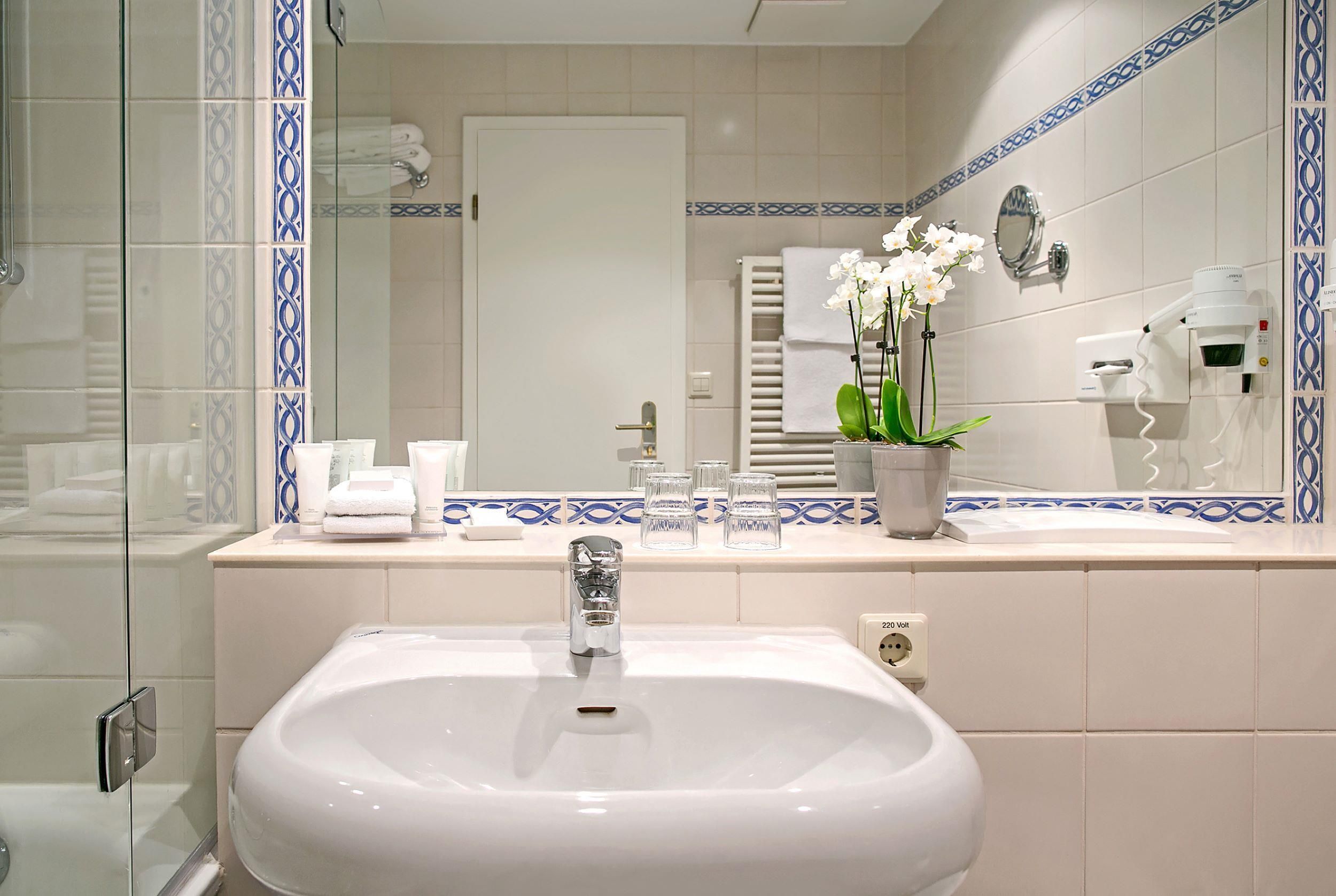 A bathroom with a white sink, a mirror, a towel rack, and a potted orchid.