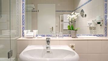 A bathroom with a white sink, a mirror, a towel rack, and a potted orchid.