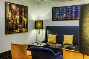 A modern hotel room with a dark blue sofa, two yellow pillows, a glass table with a lamp, and artwork on the walls. - Dorint Parkhotel Meissen (Nossen)