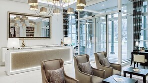 Un hall d’hôtel moderne avec un comptoir d’accueil, un espace salon, un grand miroir et un éclairage contemporain.
