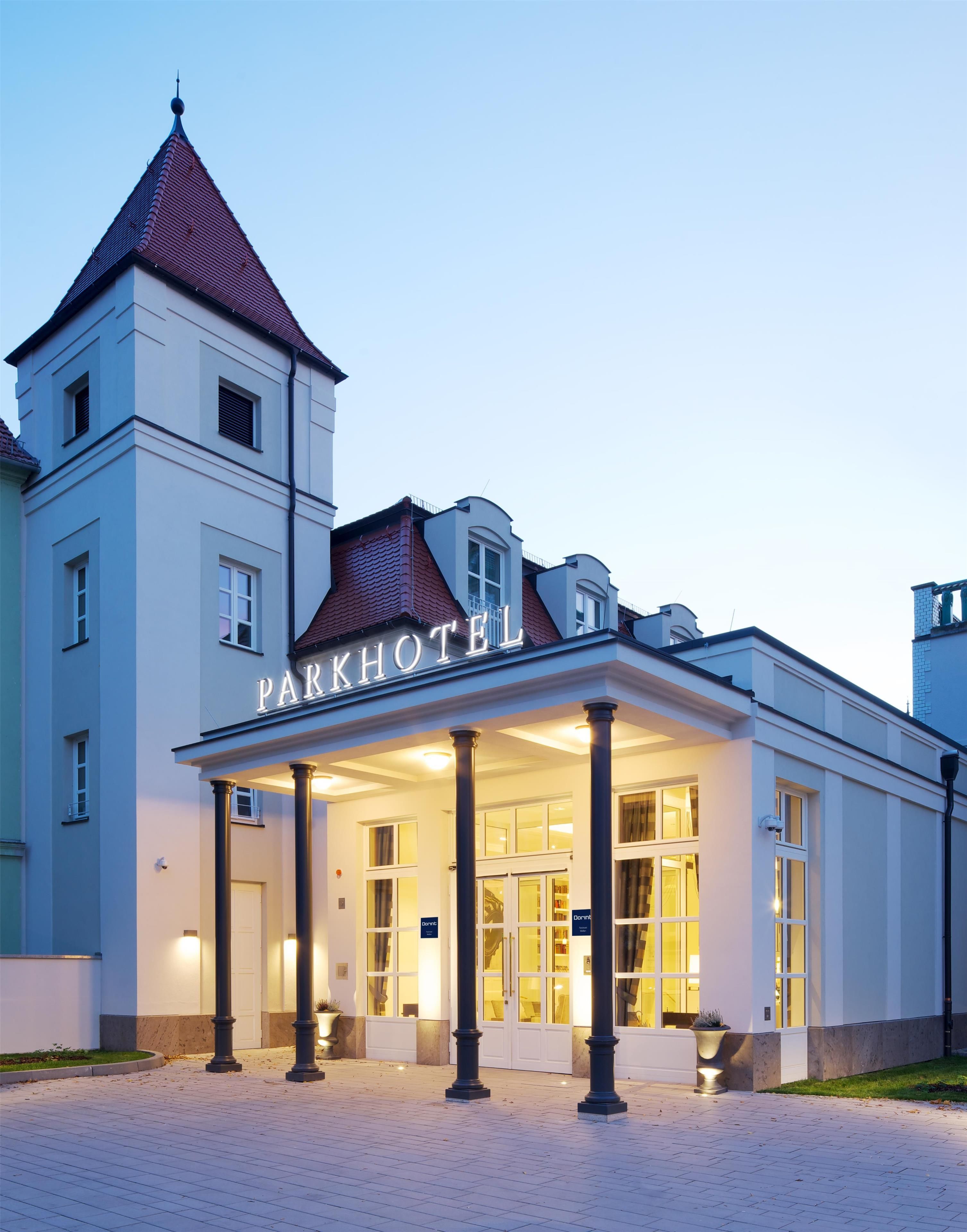 Un hôtel doté d’une entrée imposante, d’une tour et d’une enseigne sur laquelle on peut lire « PARKHOTEL ».